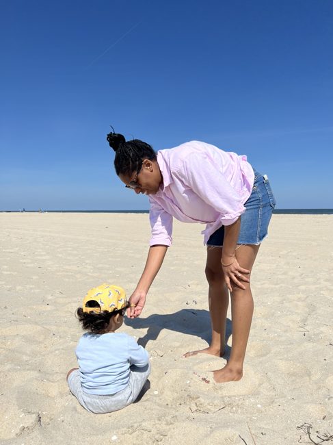 A mom and toddler playing in the sand on a bright beach day