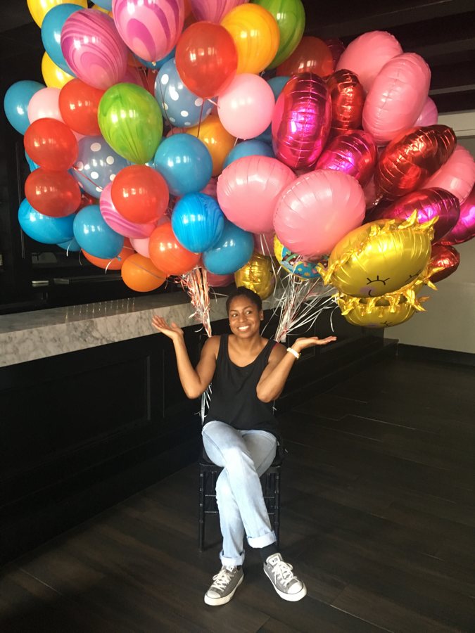 Chauntel sitting under a huge bunch of colorful balloons